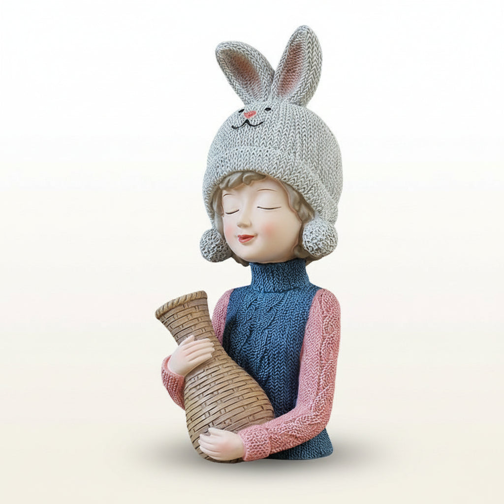 Decorative figurine of a girl wearing a knitted bunny hat holding a woven basket on a wooden surface with a gray background.