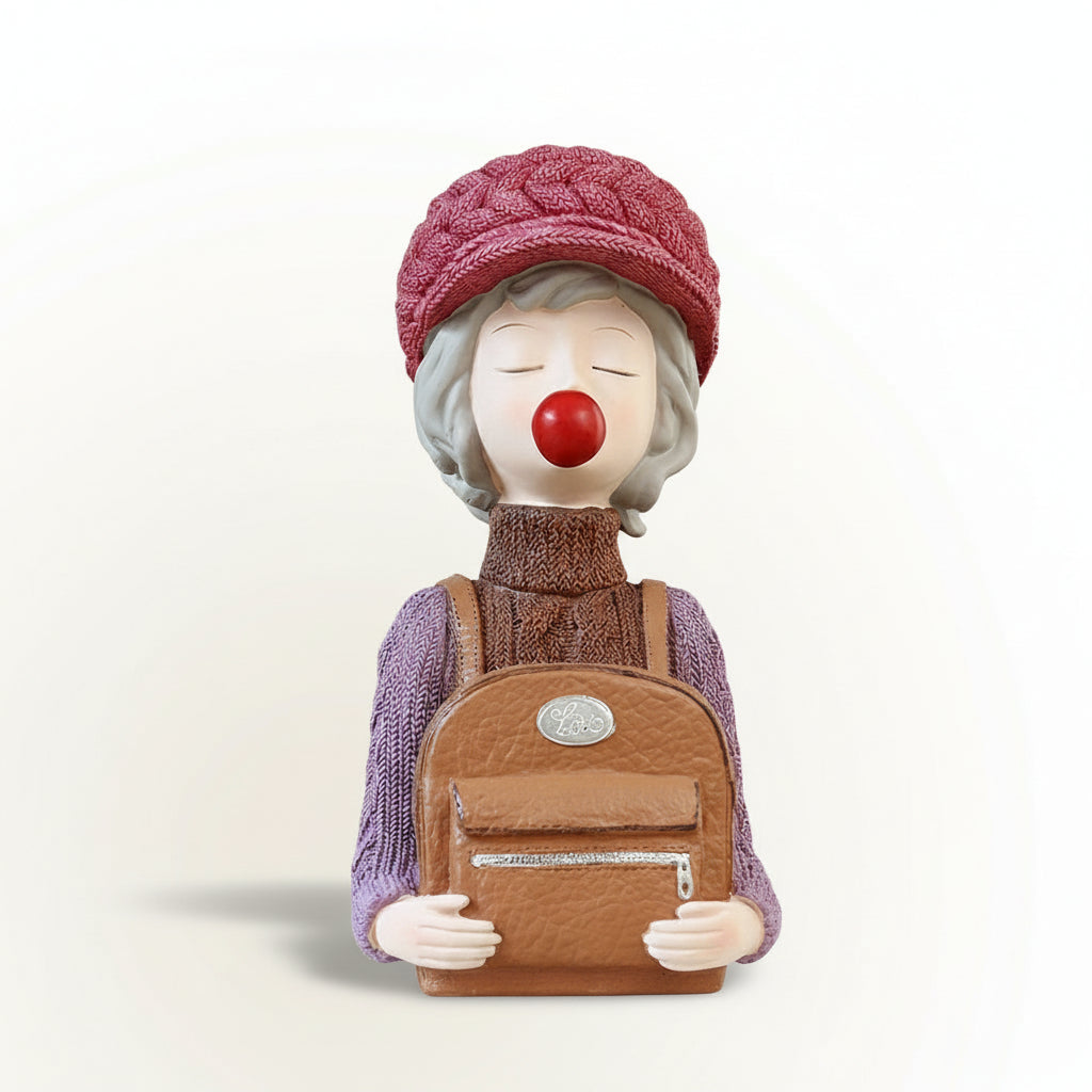 Decorative figurine of a clown with a red nose wearing a pink knitted hat and holding a brown bag.