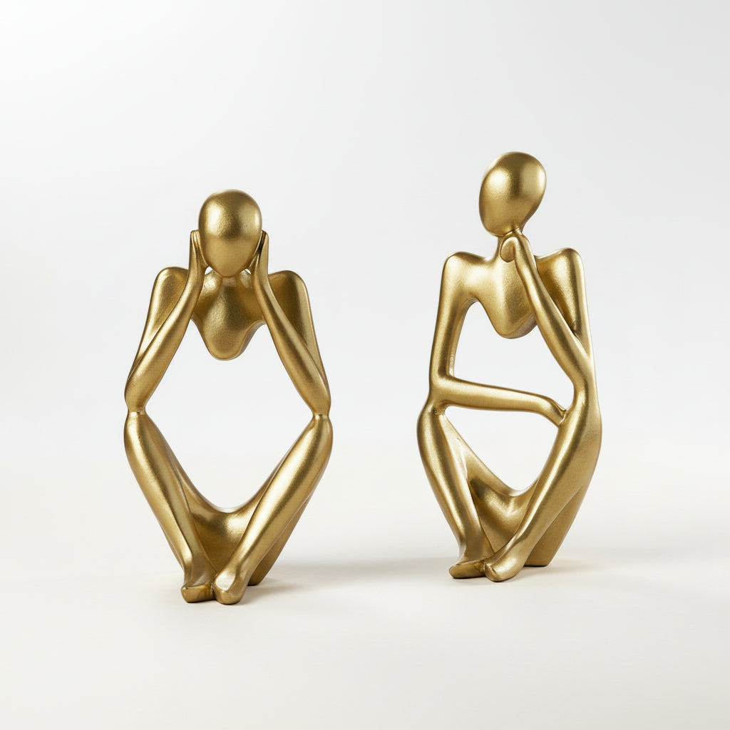 Two gold abstract sculptures on a wooden surface with a white background