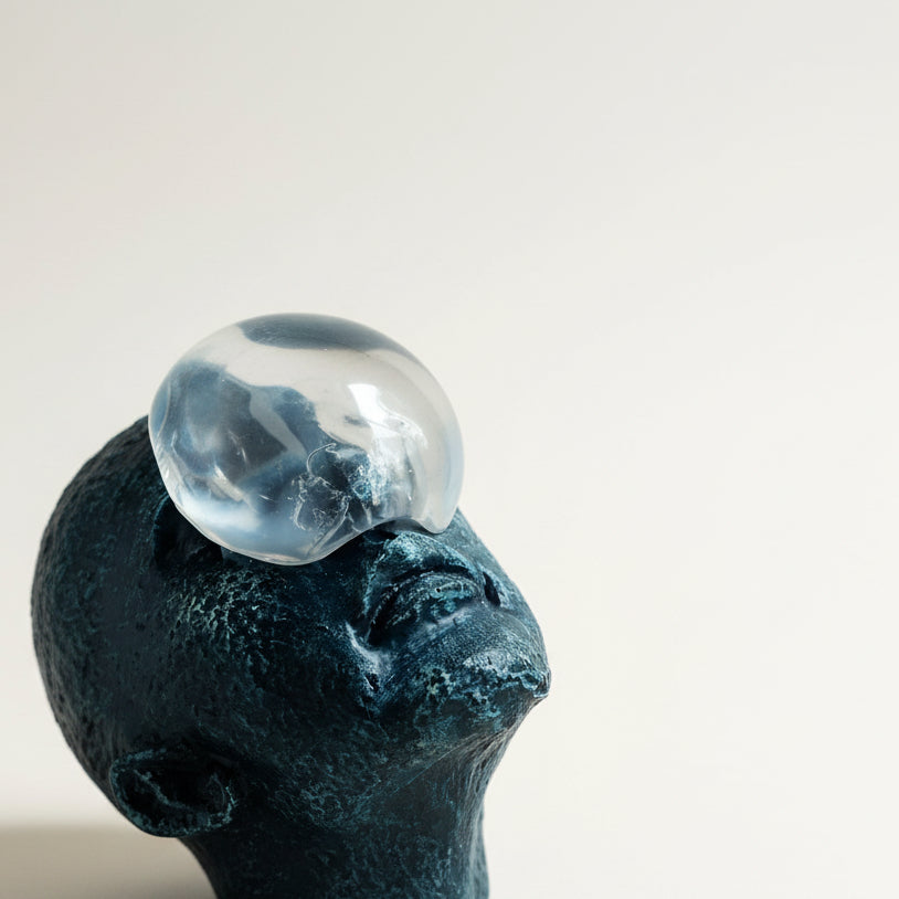 Close-up of a textured blue sculpture with a clear glass orb on top against a white background